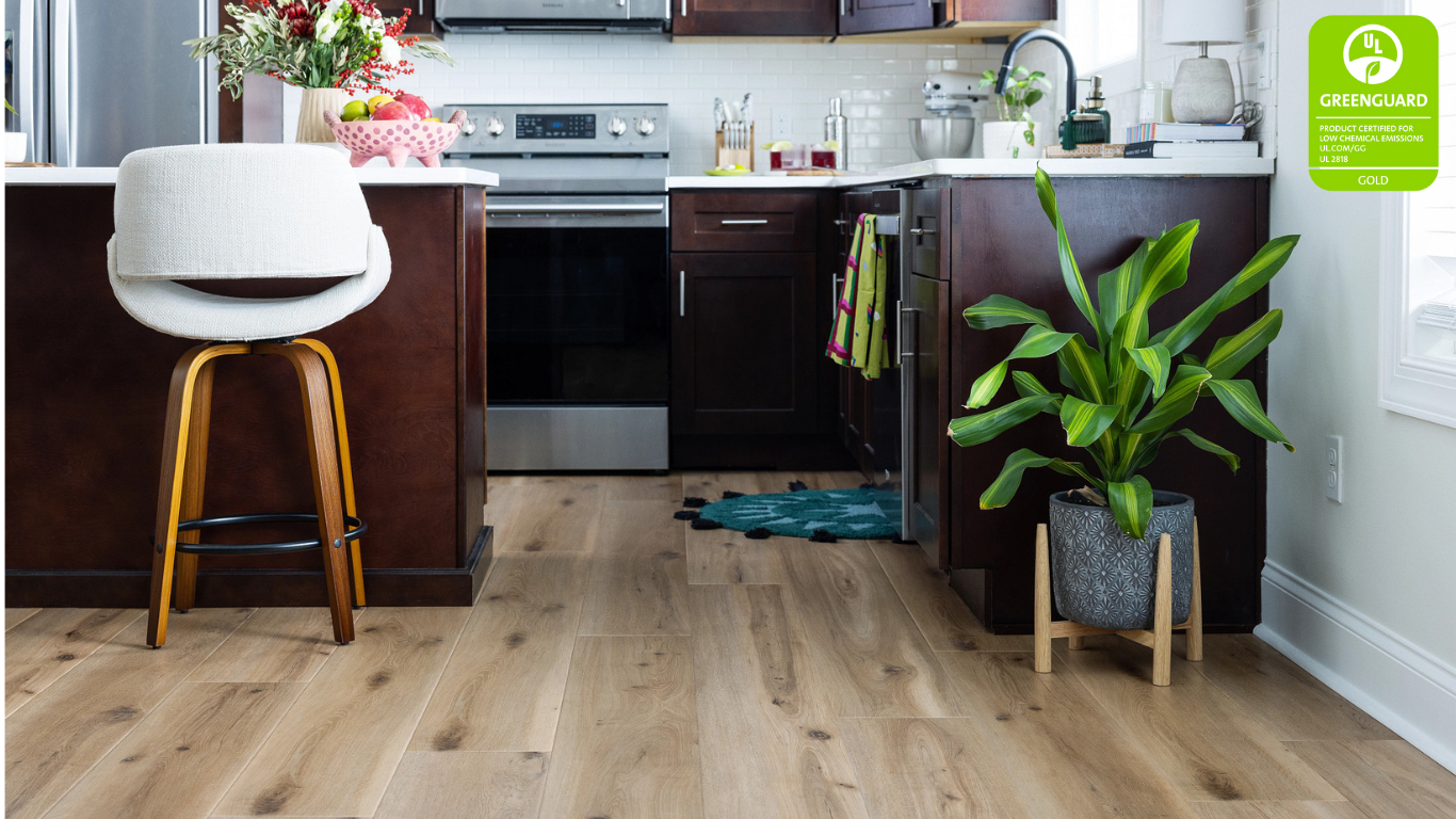 Modern kitchen with COREtec luxury vinyl plank flooring in a light oak finish, featuring rich brown cabinetry, stainless steel appliances, and a vibrant green potted plant, highlighting a GREENGUARD Gold Certification logo for safe indoor air quality.