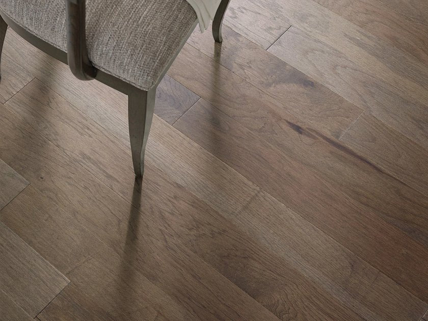 Shaw Northington Smooth Chestnut engineered hardwood flooring photographed in a dining area, pairing warm chestnut brown hardwood with dining chair legs.
