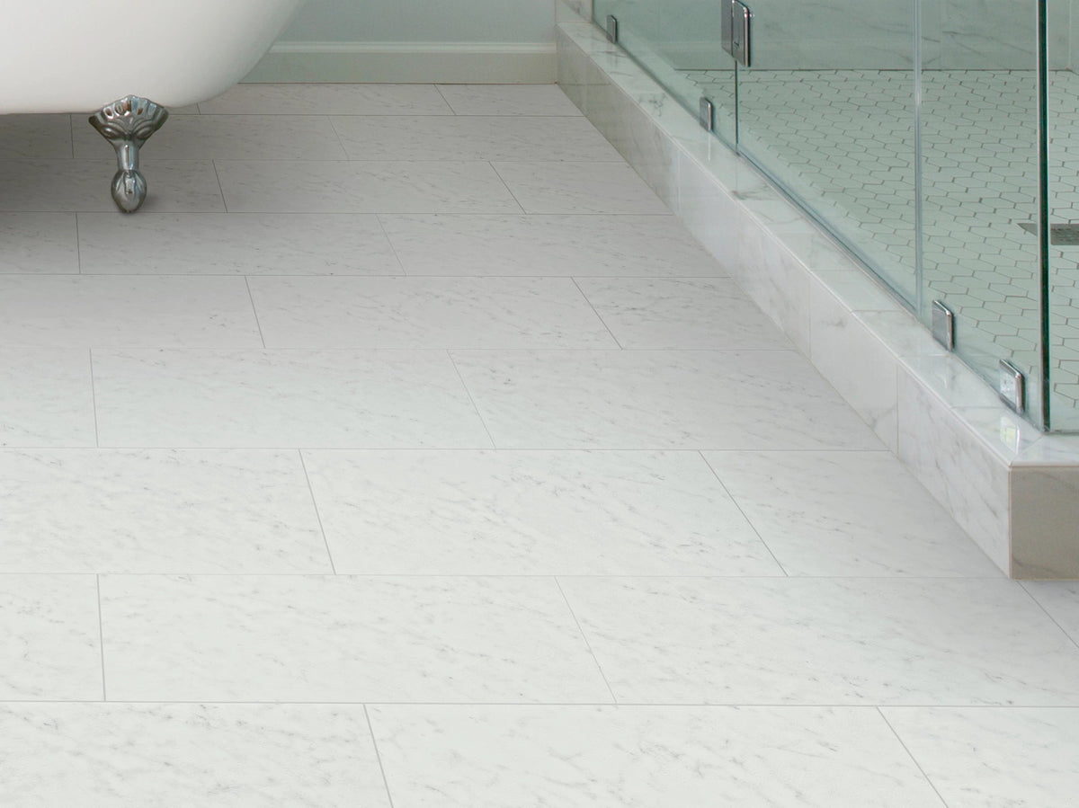 Beside a claw-foot tub and glass shower, Bianco 1022V-01217 flooring by Shaw Paragon Tile Plus displays faint gray markings in a classic white bathroom.