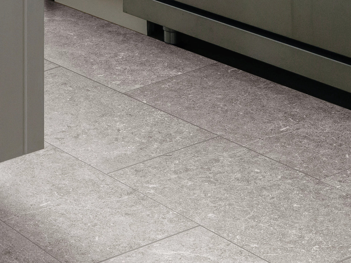 Pewter 1022V-05260 tiles from Shaw Paragon Tile Plus show cloudy gray variation at a kitchen doorway, bordered by neutral cabinetry and a metal appliance base.