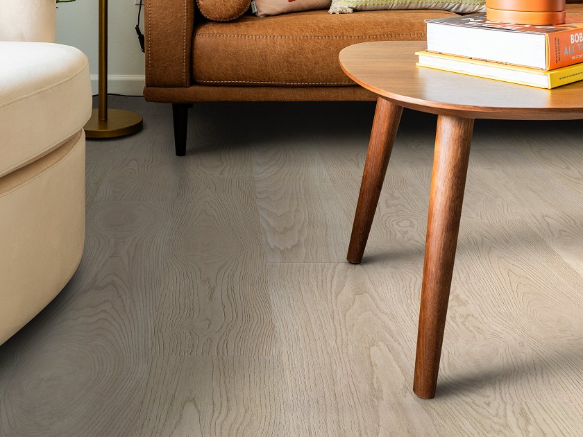 Shaw Fresh Take Shell Taupe wood-look vinyl planks show cool gray-beige coloring and sweeping grain curves in a seating area with a sofa, curved armchair and round side table.