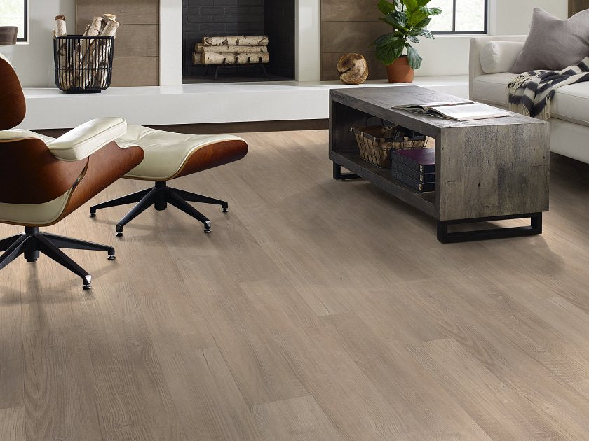 A fireplace and leather lounge chair surround Shaw Endura Plus Simple Wash 0736V-02083 vinyl flooring, its taupe wood-look pattern visible across the room.