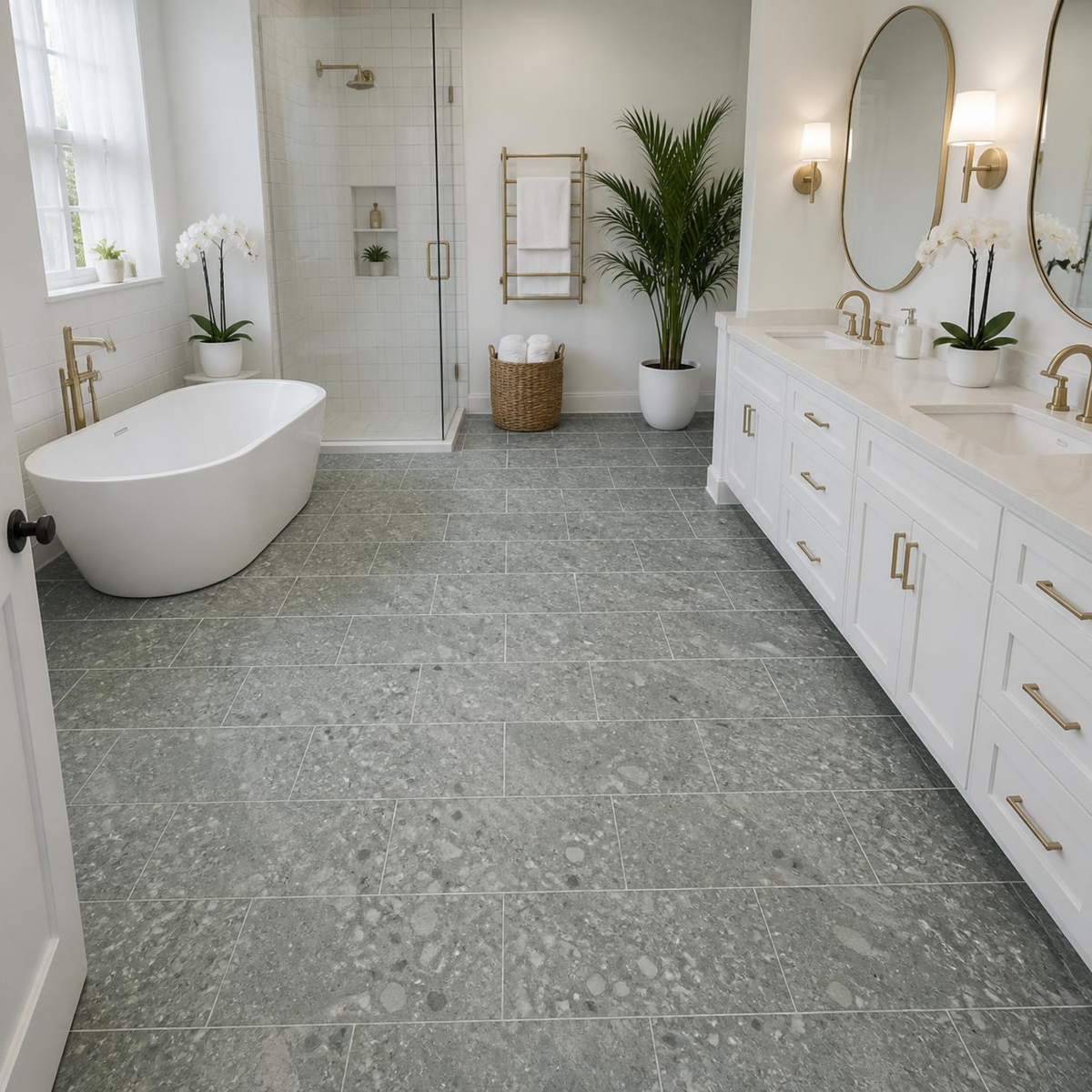 Bathroom with a freestanding white tub, a glass-enclosed shower, a white double vanity with brass hardware and oval mirrors, a potted palm, and a towel warmer over Armstrong Alterna Lost Empire Desert Mist D4021 16x16 vinyl tile flooring.