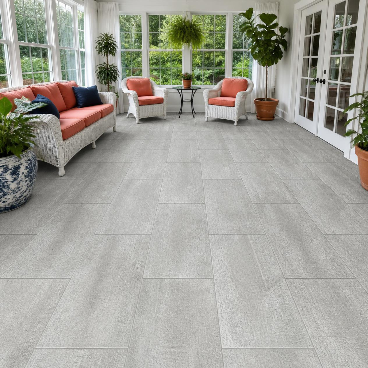 Sunroom with a white wicker sofa and armchairs with coral cushions, navy pillows, French doors, large windows, and potted plants over Armstrong Alterna Grain Directions Coffee Milk D7364 12x24 vinyl tile flooring.
