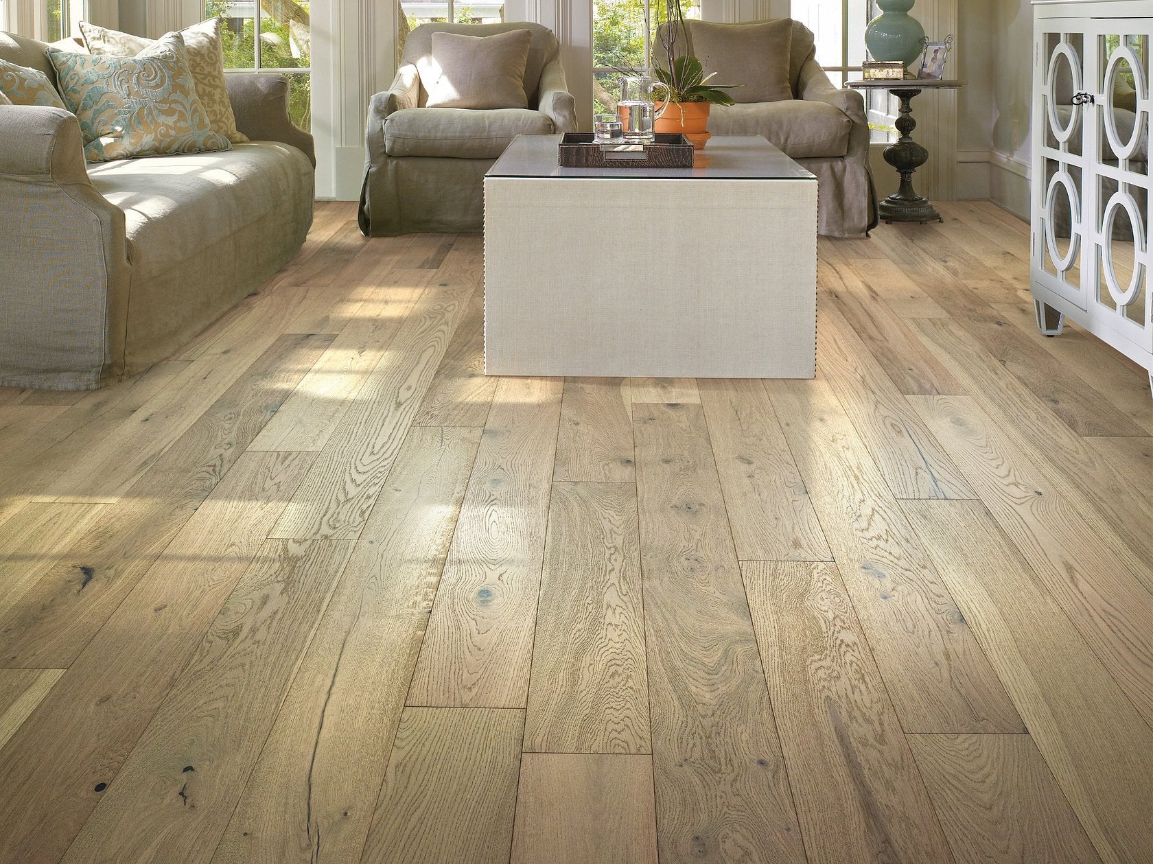 Living room view of Shaw Couture Oak Crema engineered hardwood flooring, showing light creamy oak hardwood color near sofa seating and the open floor area.