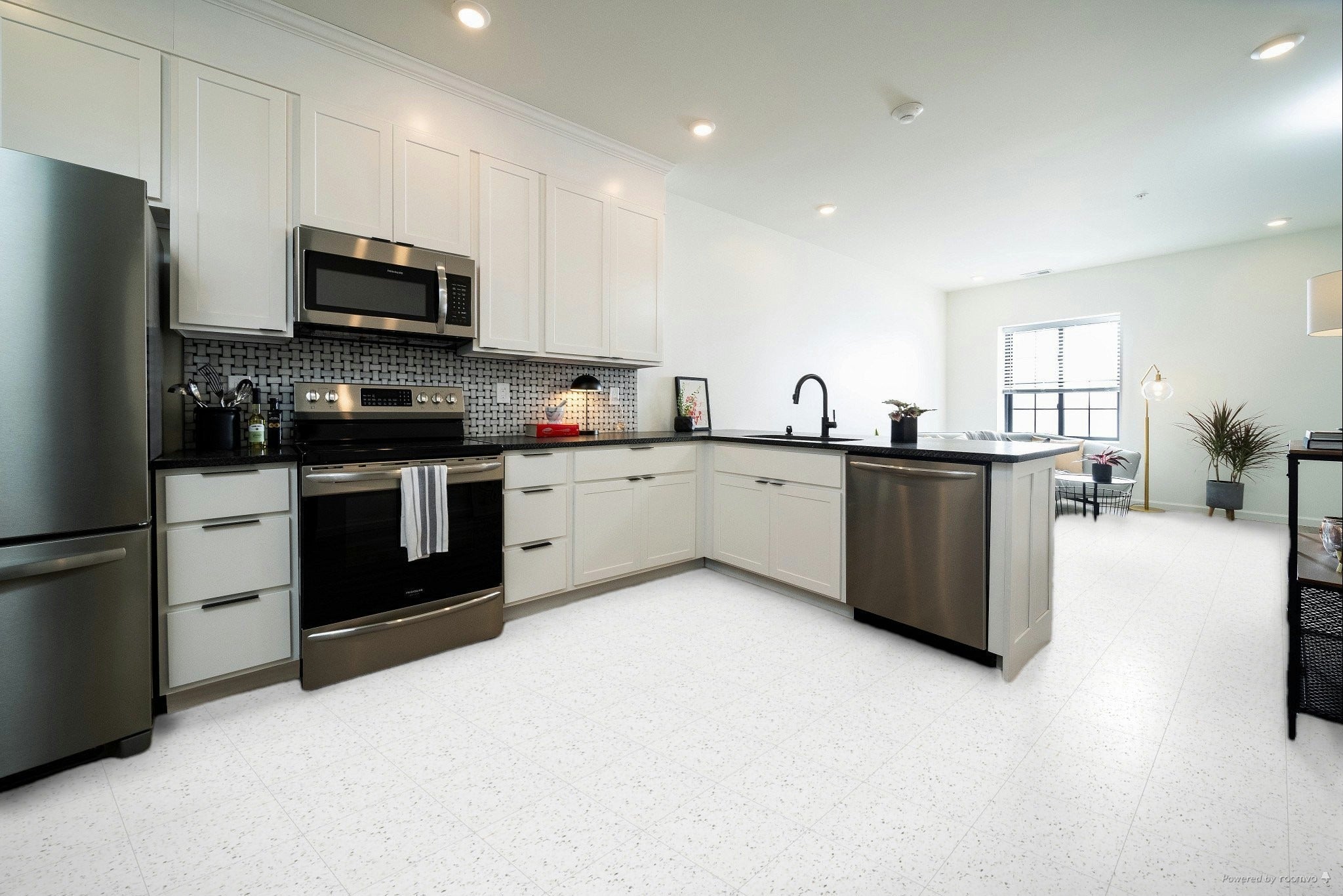 Modern kitchen with Armstrong VCT tile flooring in a white speckled pattern. The space features white cabinetry, stainless steel appliances, black countertops, and a stylish mosaic backsplash, flowing into an open-concept living area.
