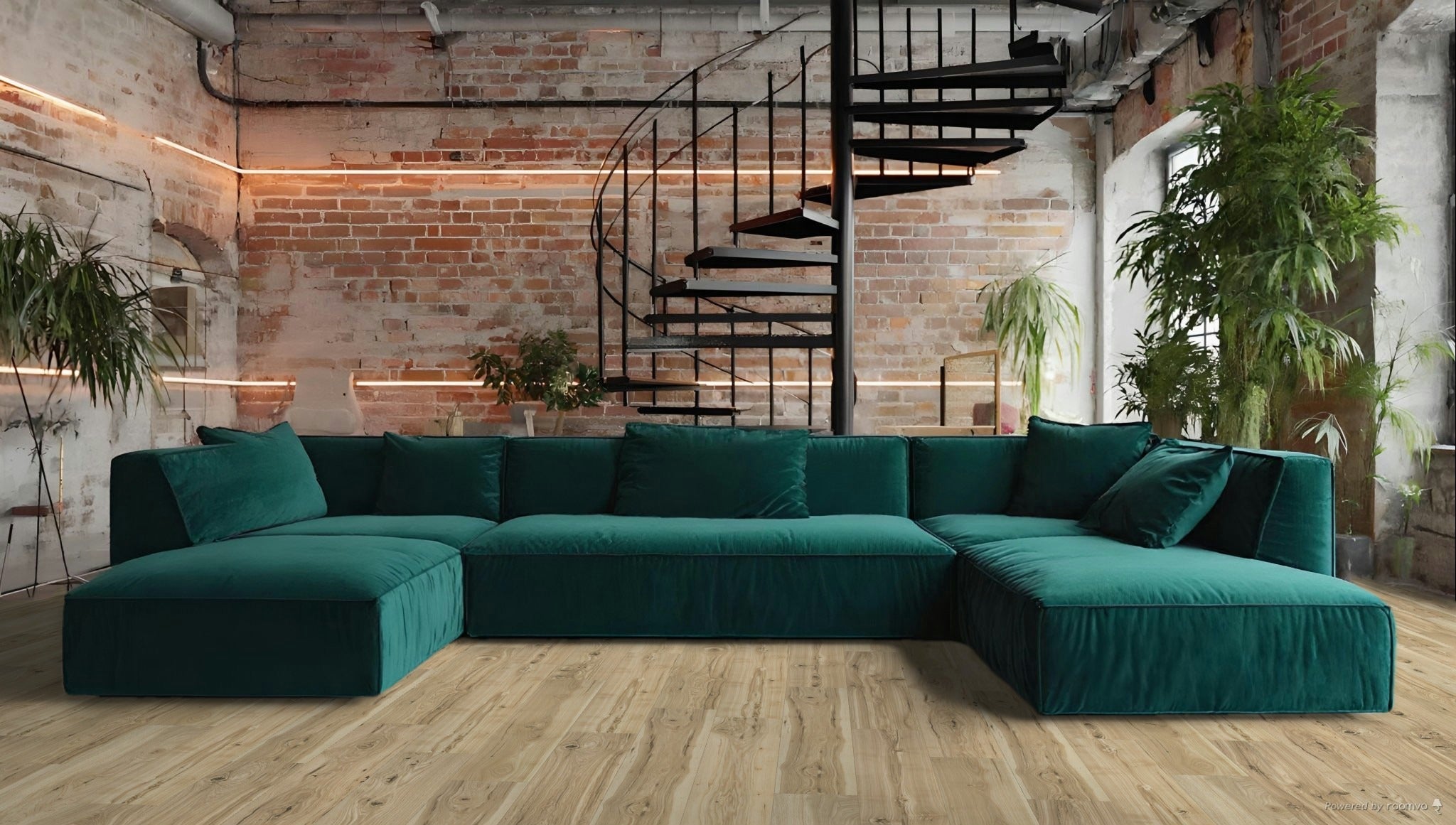 A modern teal sectional sofa with plush cushions in an industrial-style room featuring exposed brick, plants, and a spiral staircase.