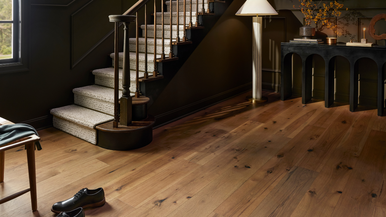 Luxury hardwood flooring in an elegant home entryway featuring warm-toned wide-plank wood floors, a modern staircase with textured carpeting, and sophisticated decor.