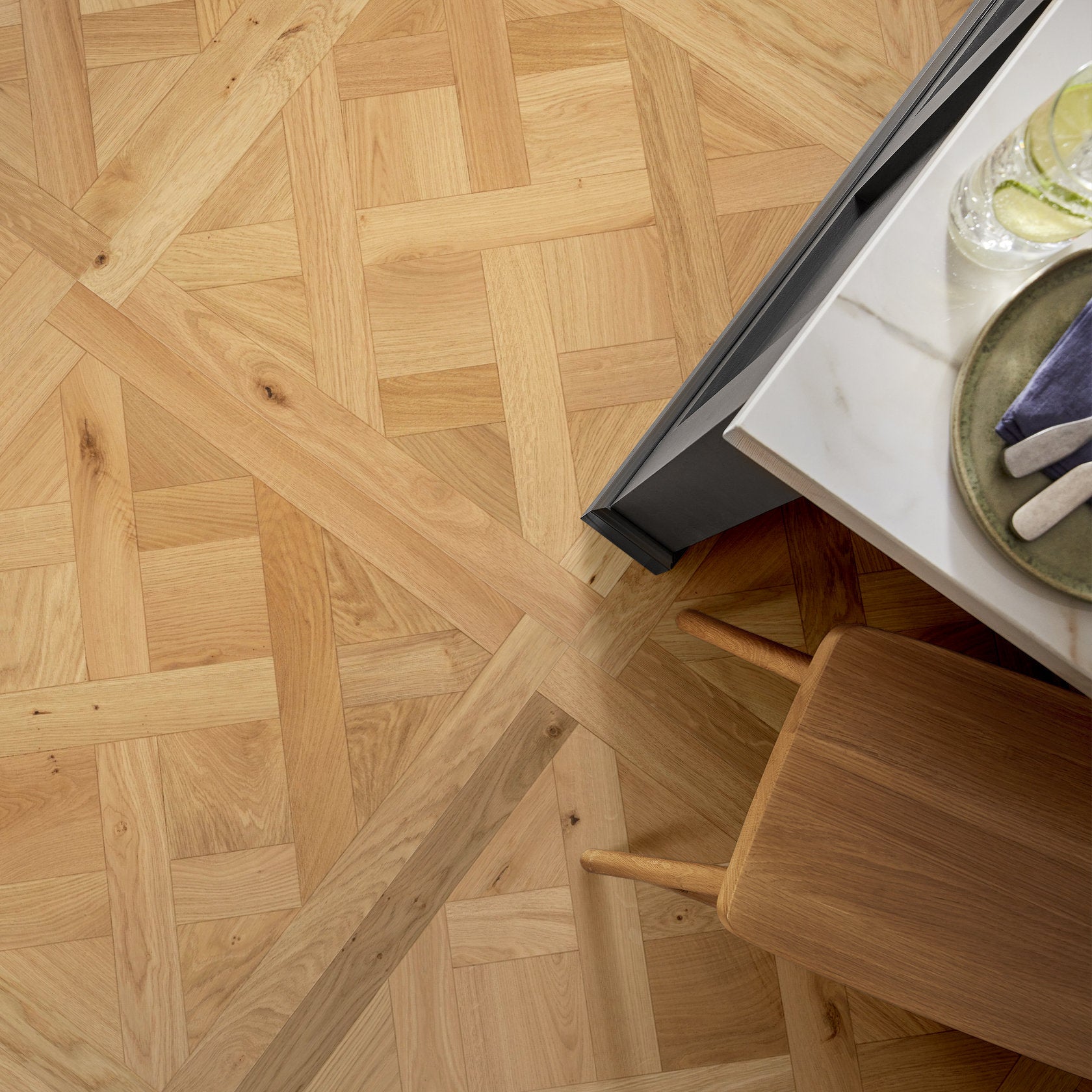 Close-up view of Anderson Tuftex Provincial Parquet white oak hardwood flooring featuring 31.5-inch square panels in a classic parquet pattern beside a dining table and chair.
