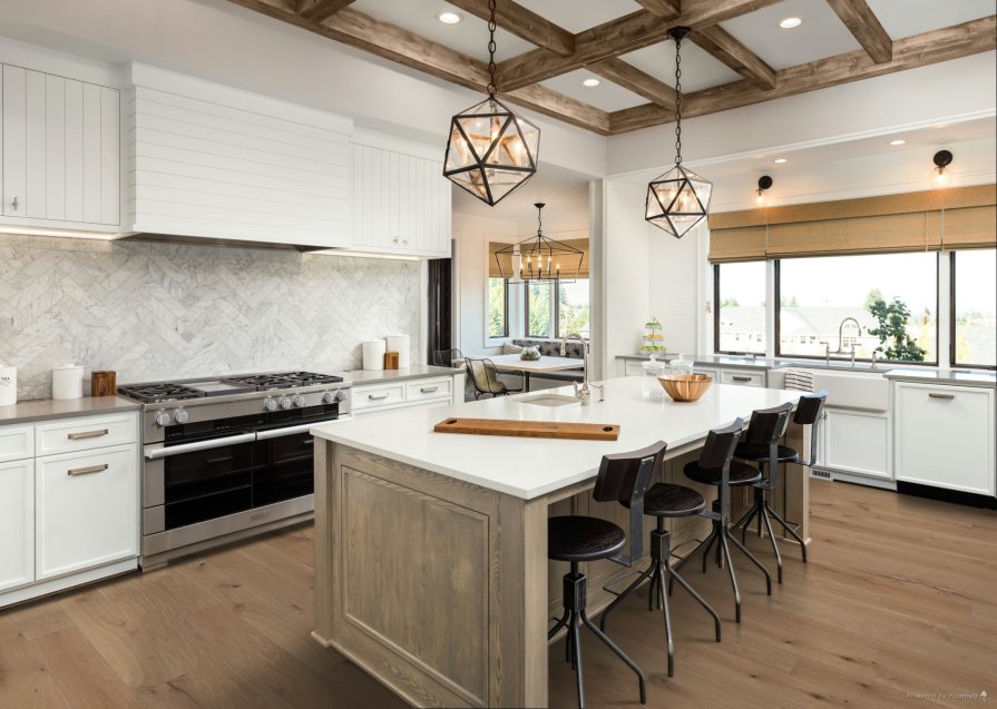 Modern kitchen interior featuring Anderson Tuftex Provincial Plank wide white oak hardwood flooring, white shaker cabinets, wooden ceiling beams, quartz island countertop, and pendant lighting over a central island with barstools.