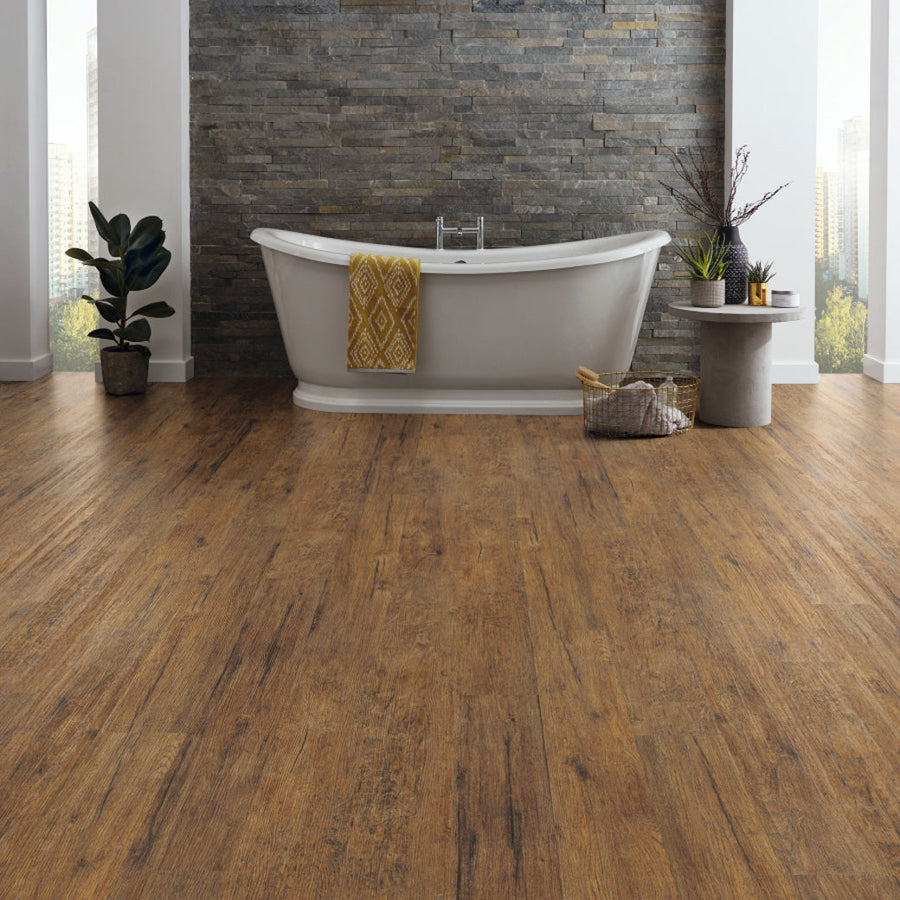 A modern bathroom featuring a freestanding tub, karndean korlok reserve vintage oregon oak flooring, a stone accent wall, and decorative plants and accessories.