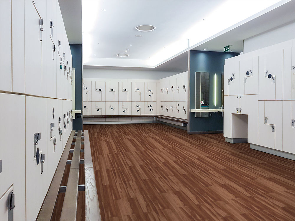 Clean locker room with brown wood-look flooring and white lockers under bright ceiling lights.