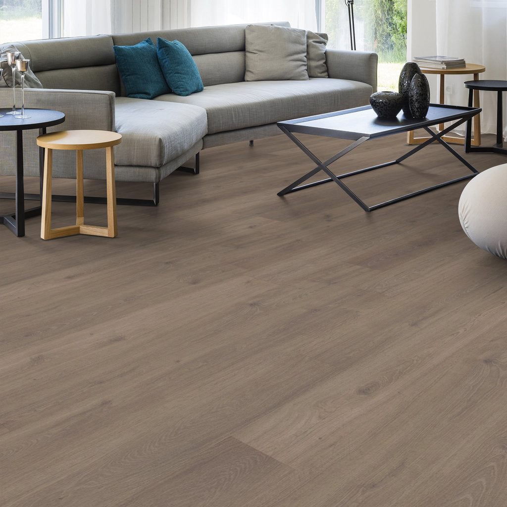 A modern living room features a gray sofa with blue cushions, a wooden side table, a sleek black coffee table, and Shaw Oak Crest Northwood Gray Laminate flooring.
