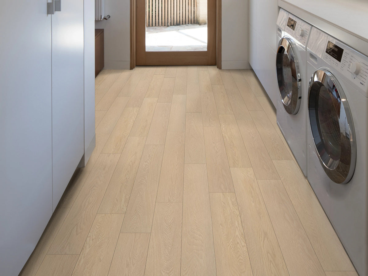 Between blue cabinets and front-loading laundry appliances, Shaw Paladin Plus Oceanfront (0278V-02012) leads toward a glazed door, bringing a golden wood look to the modern utility room.