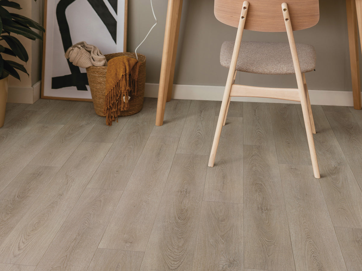 Curved oak-style figuring, instead of a strongly linear pine look, appears beneath a light wood chair in the Scandinavian-style workspace showing Shaw Paladin Plus Toasted Taupe (0278V-05218). Talk through Toasted Taupe's room view with Floor City before deciding.