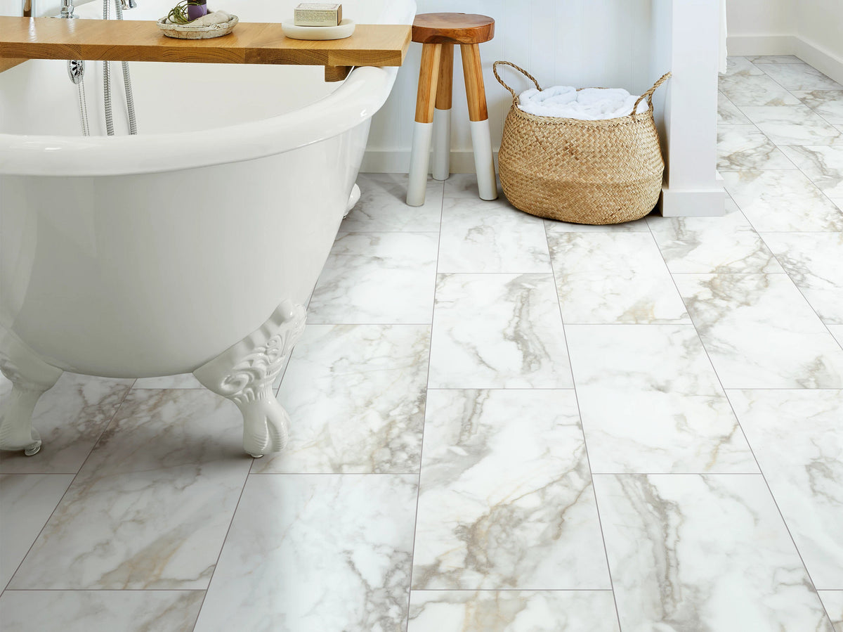 A woven laundry basket and wooden bath tray accompany Calacatta 1022V-01100 from Shaw Paragon Tile Plus, with gold-gray veining around a white claw-foot bathtub.