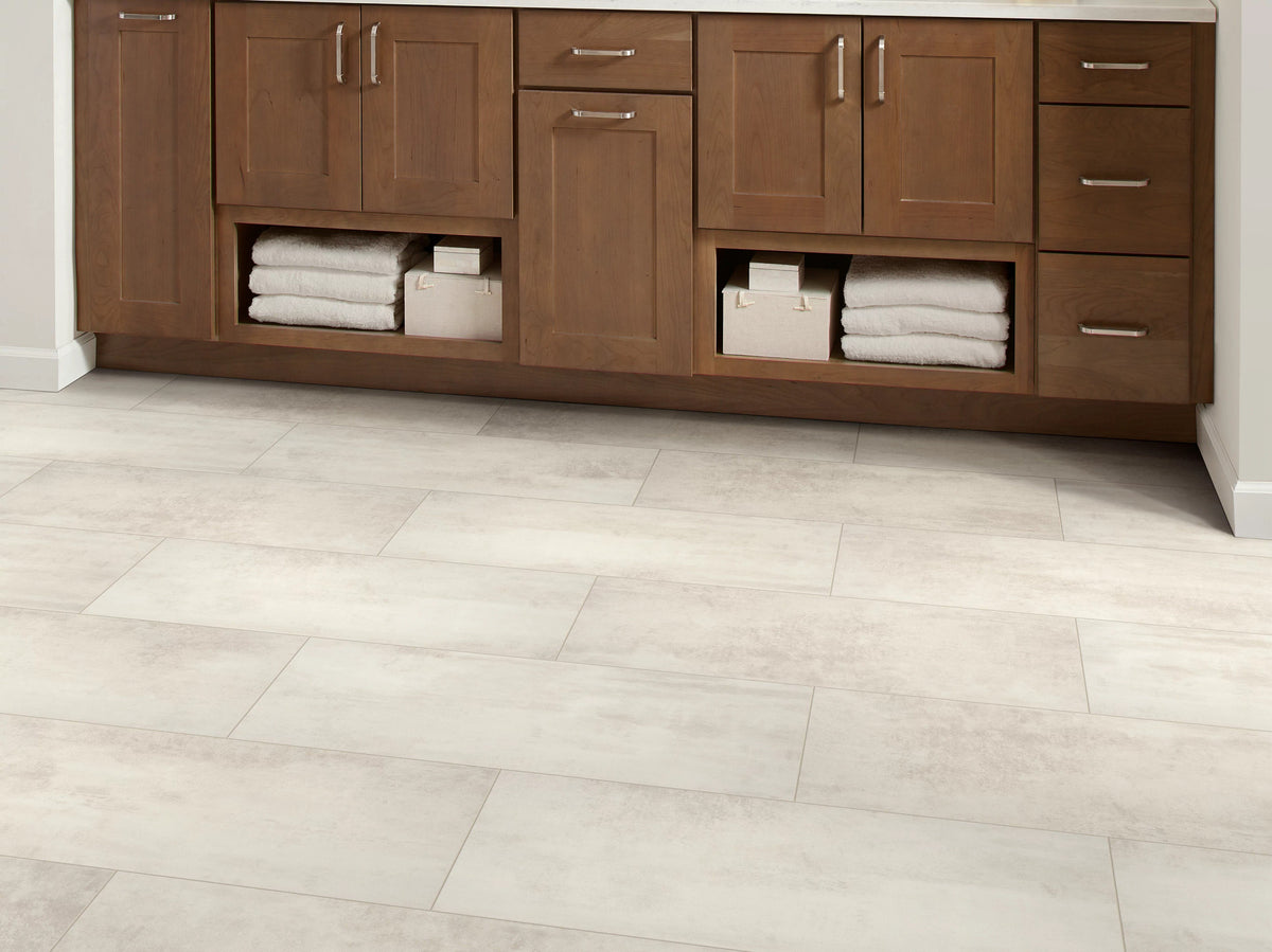 A warm wood bathroom vanity with open towel shelves sits over Bone 1022V-01125 by Shaw Paragon Tile Plus, creating a subdued transitional setting.