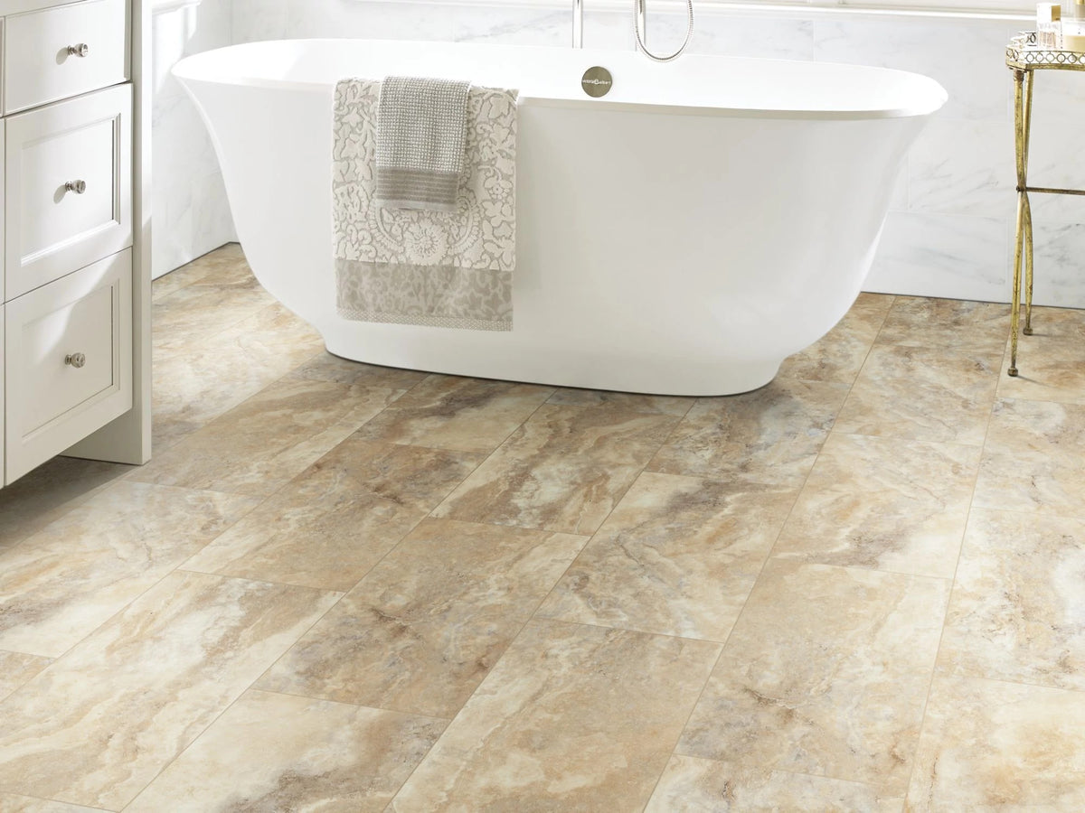 A freestanding white bathtub, patterned towel and brass-toned stand accompany Clay 1022V-07052 by Shaw Paragon Tile Plus, creating a warm contemporary bathroom.