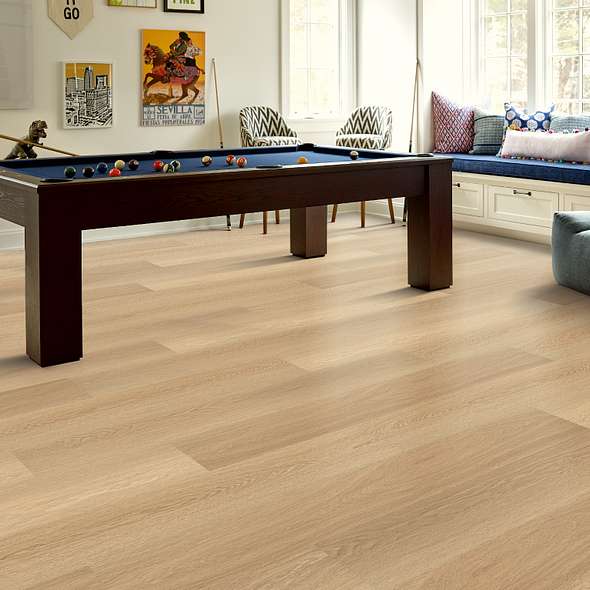 Around a pool table in a game room interior, Shaw Endura Plus Castaway 0736V-07087 wood-look vinyl planks appear light golden tan.