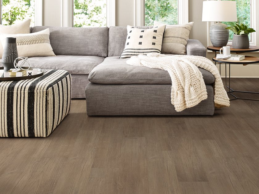 Long plank rows extend toward a gray sectional in this living room with muted brown Shaw Endura Plus Casual Comfort 0736V-07294 vinyl flooring.
