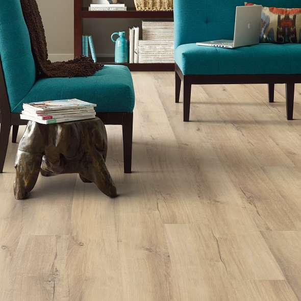 Scattered knot markings punctuate light tan Shaw Endura Plus Marina 0736V-02014 vinyl planks beneath teal chairs in a sitting room.