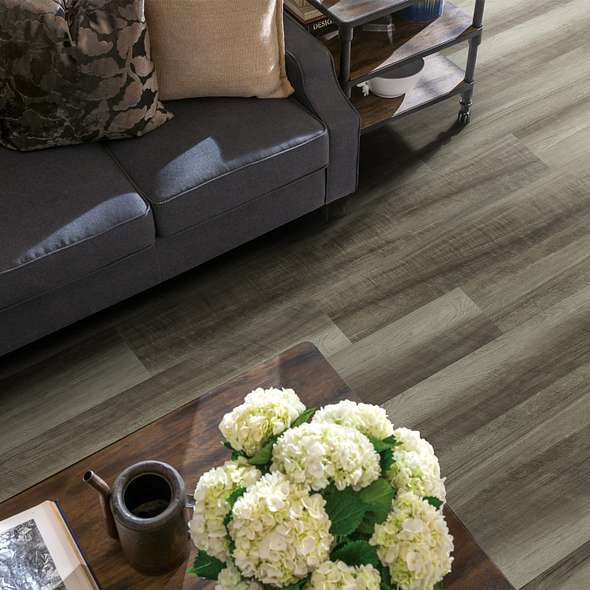 Alternating gray-brown shades distinguish Shaw Endura Plus Oyster Oak 0736V-00591 vinyl boards beside a dark sofa in an overhead living-room view.