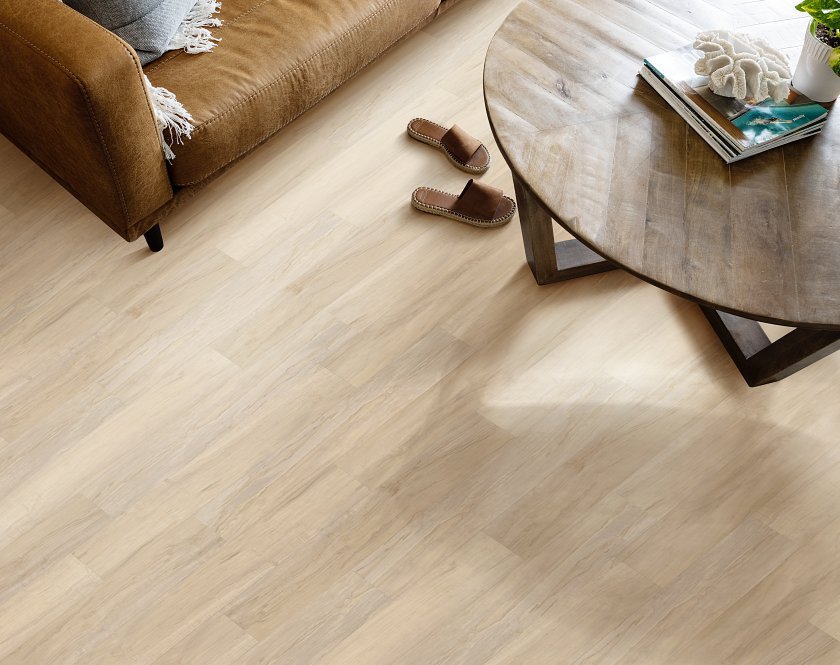 Pale beige planks show thin brown grain lines beside a tan sofa: Shaw Endura Plus Spalted Maple 0736V-02084 vinyl, seen from overhead.